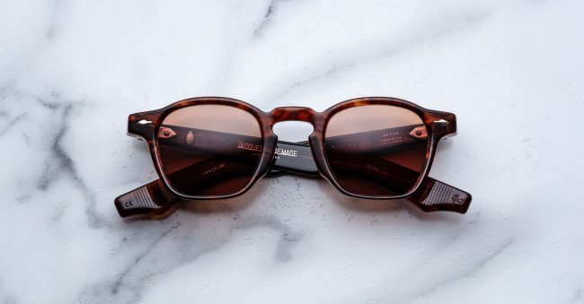 The Jacques Marie Mage Zephirin sunglasses, featuring a brown tortoiseshell square frame and dark lenses, are displayed with folded arms on a white marble surface.
