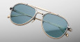 The Jacques Marie Mage 755M are aviator-style sunglasses with a gold metal frame, blue-tinted lenses, thin temples, and a double-bar bridge, displayed against a plain light gray background.