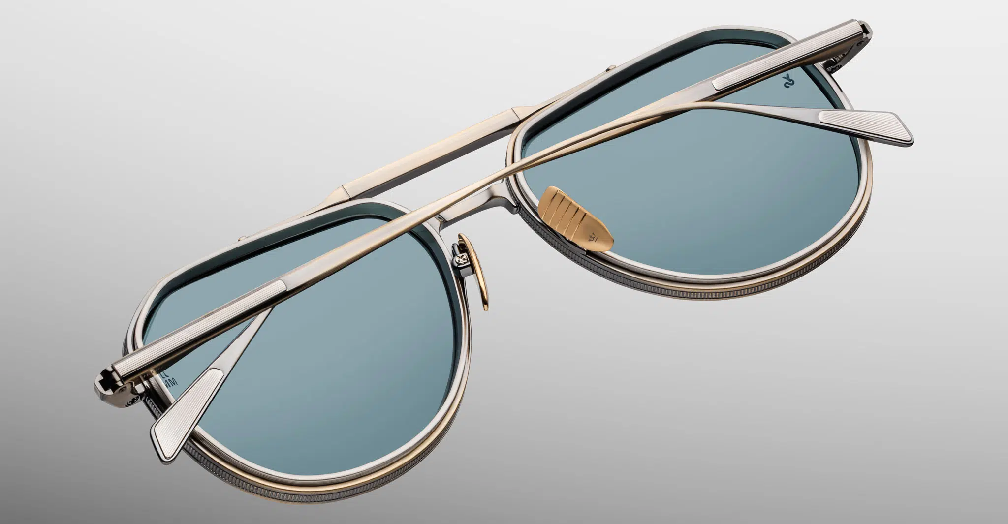 A close-up of the Jacques Marie Mage 755M sunglasses showcases their blue-tinted lenses and metallic frame from the back, highlighting the temples, hinges, and nose pads against a neutral background.