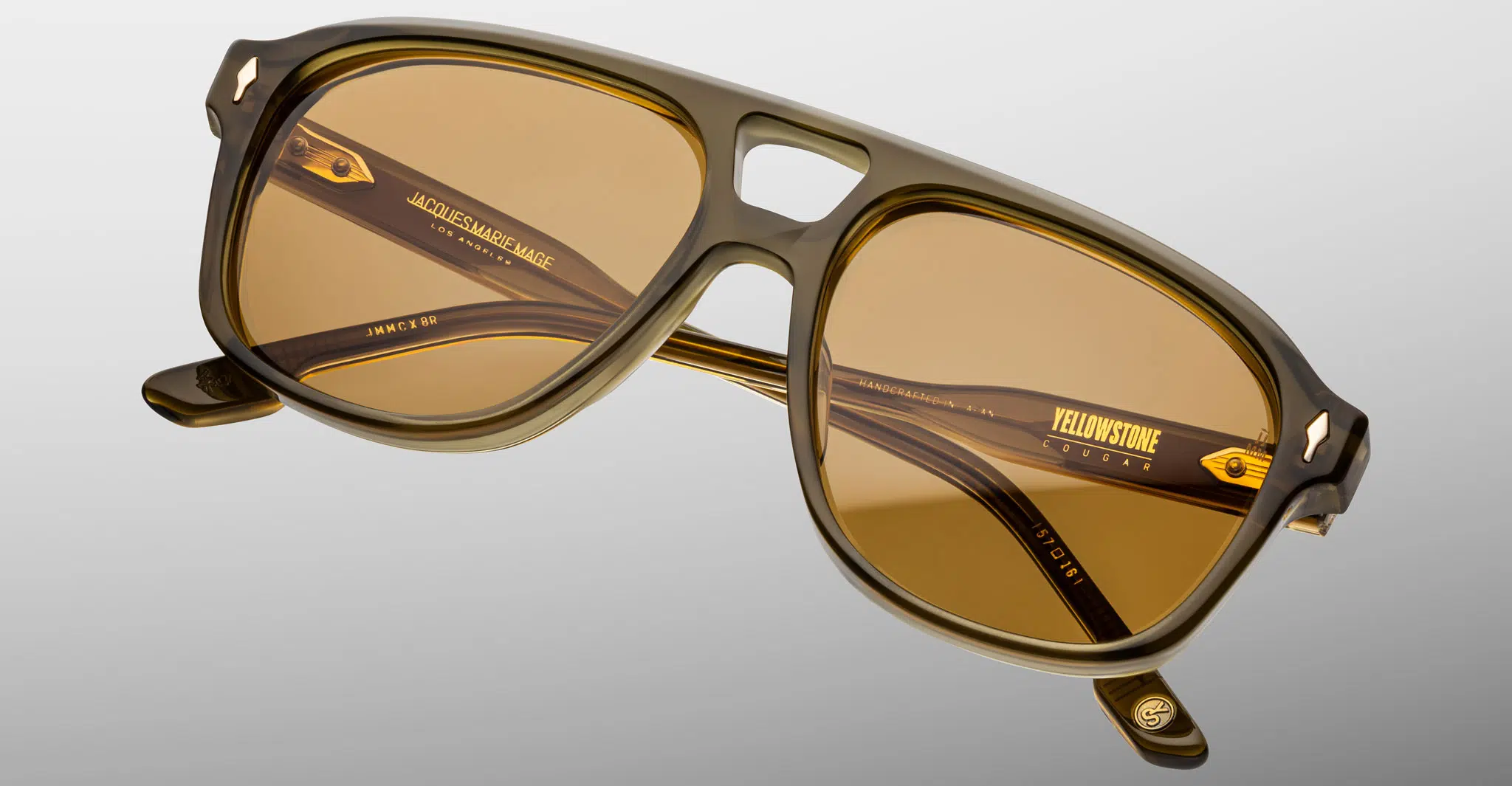 A pair of Jacques Marie Mage Cougar sunglasses featuring a thick, glossy brown rectangular frame with amber lenses and a keyhole bridge. Gold branding and model info appear on the inside of the arms.