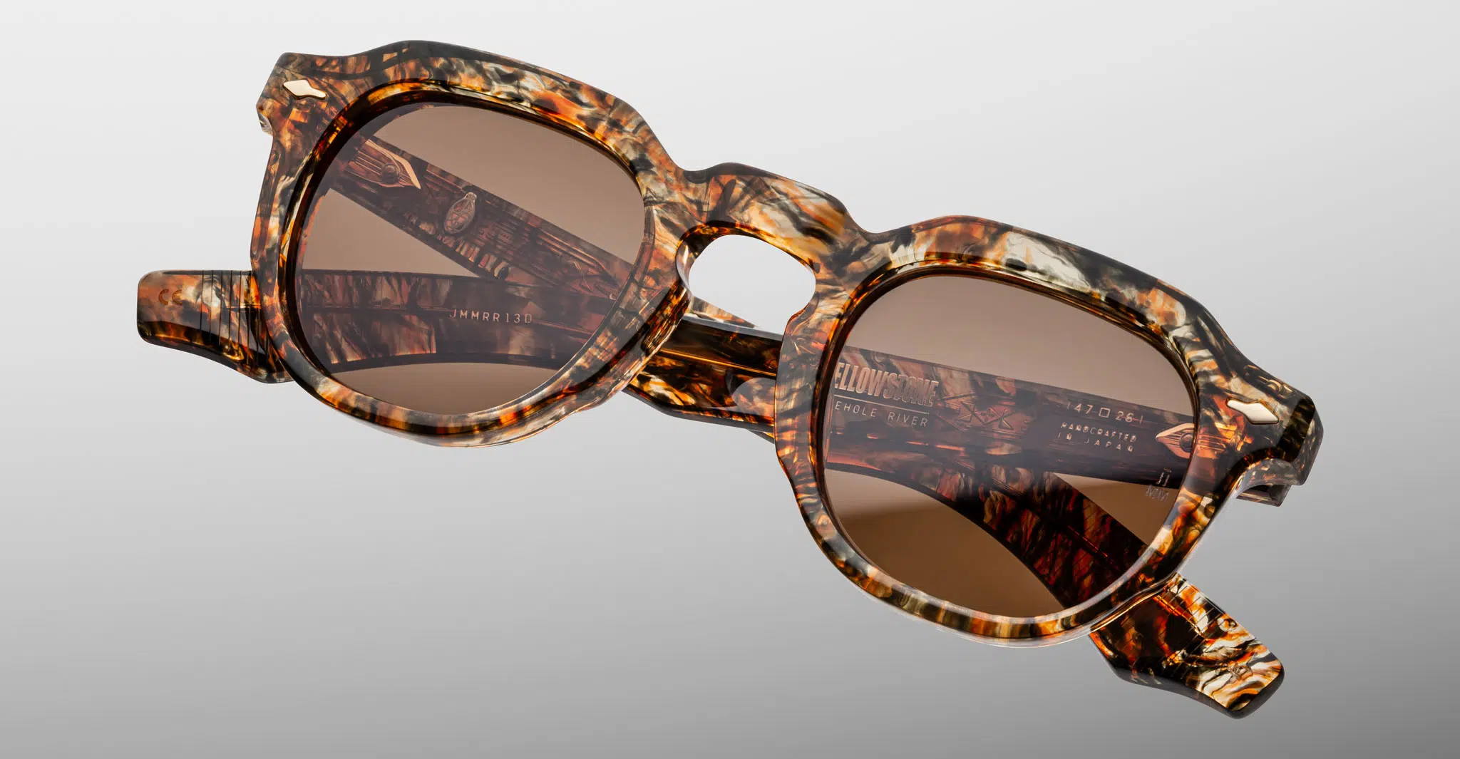 The Jacques Marie Mage Firehole River sunglasses feature thick, marbled brown and beige rectangular frames with brown tinted lenses, shown against a neutral gray background.
