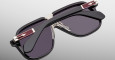 The Jacques Marie Mage Kurokawa sunglasses feature a stylish black frame with gold accents on the arms, shown folded and resting on a light gray surface.