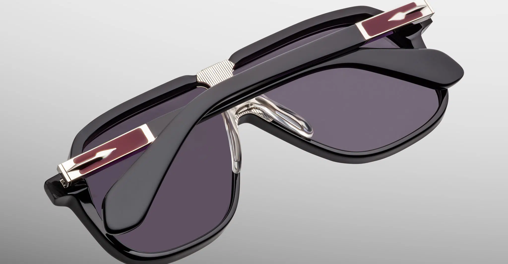 The Jacques Marie Mage Kurokawa sunglasses feature a stylish black frame with gold accents on the arms, shown folded and resting on a light gray surface.