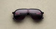 The Jacques Marie Mage Kurokawa sunglasses, featuring a large black aviator design with dark lenses, rest on a beige textured surface.