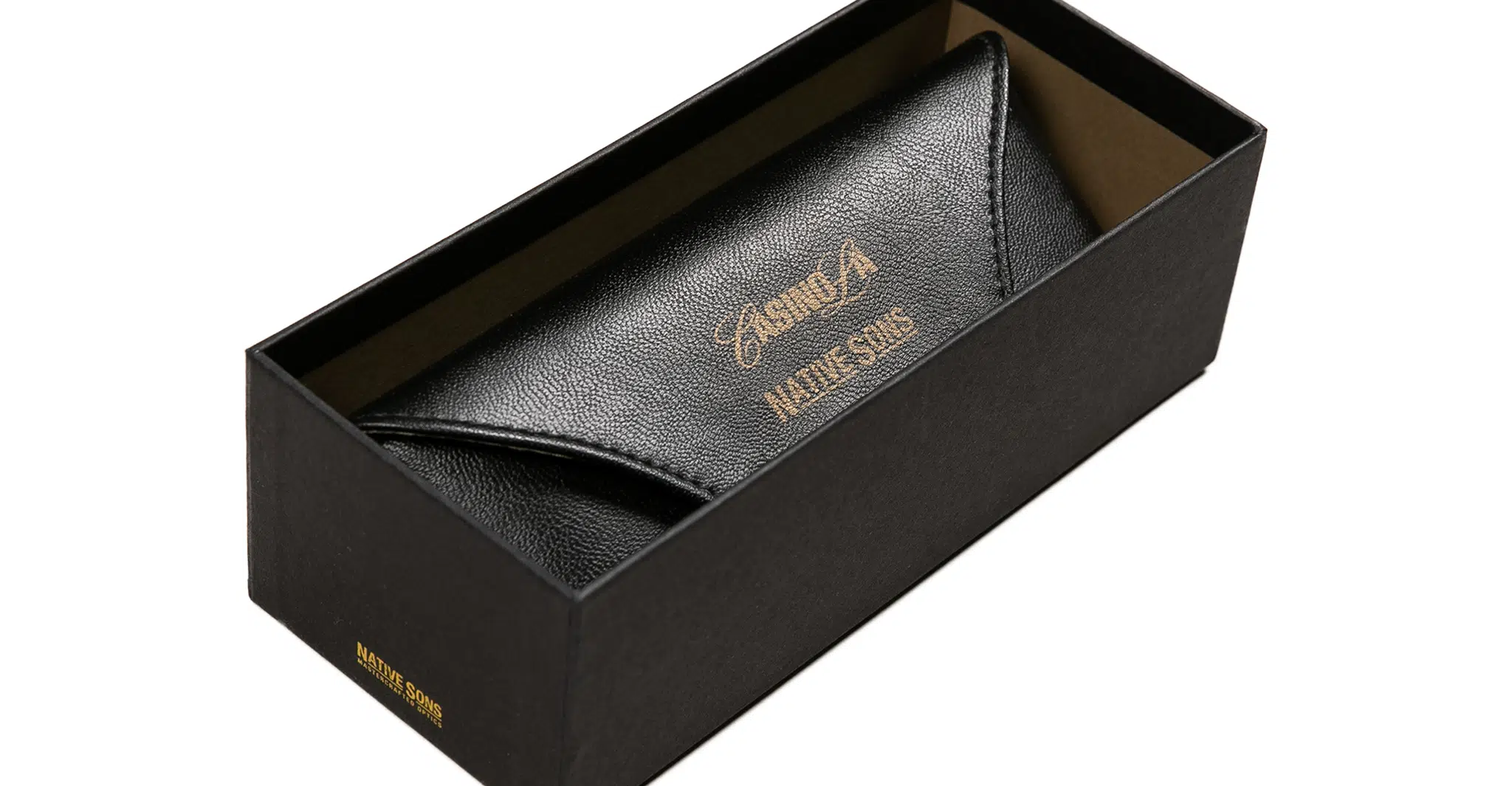 The Native Sons x Casinola "The E's" features a sleek black leather eyeglasses case adorned with gold text, elegantly displayed inside an open black rectangular box for a sophisticated presentation.