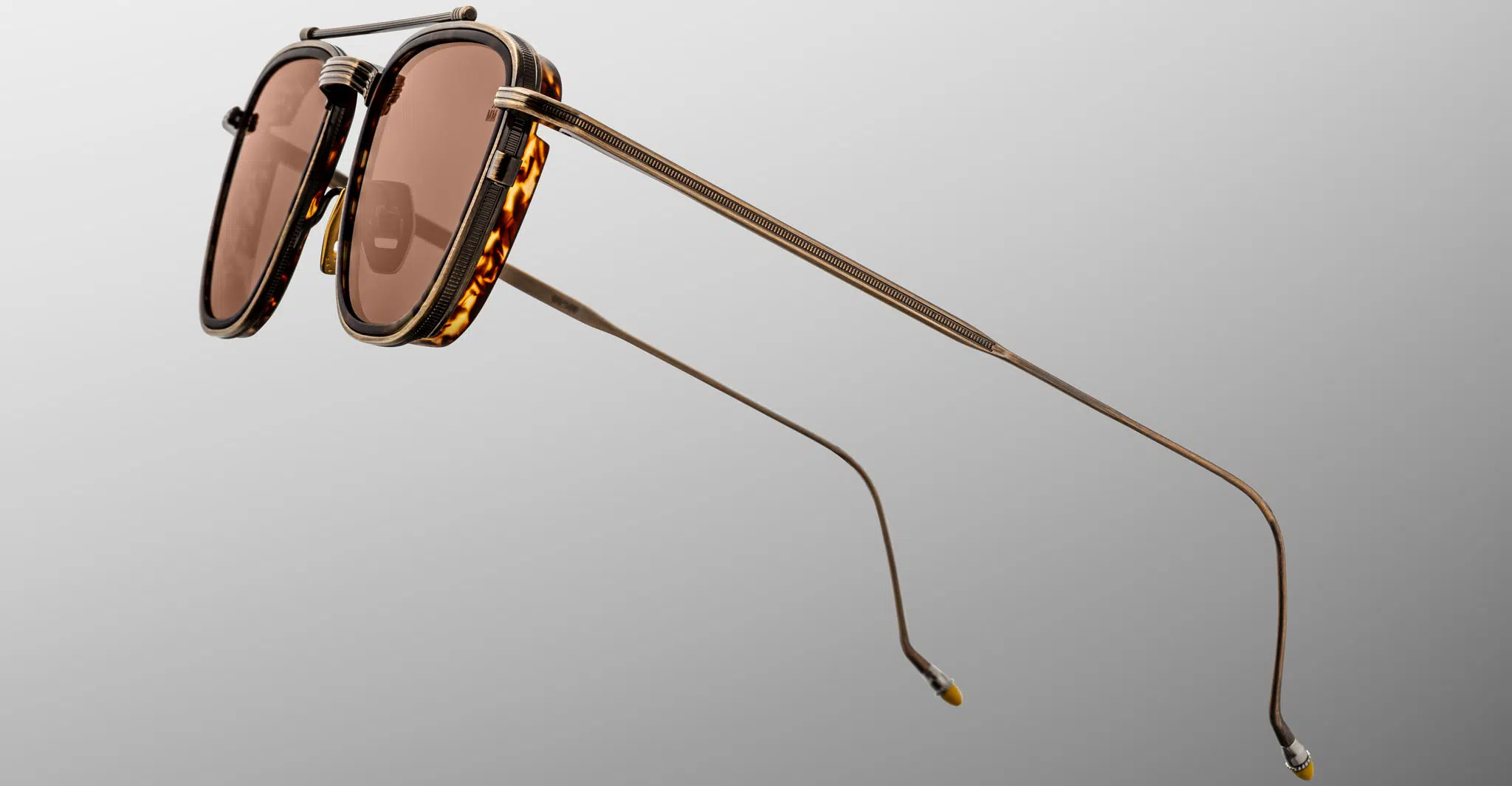 Jacques Marie Mage 1992 sunglasses feature tortoiseshell frames, rose-tinted lenses, and slim gold metal arms, shown against a neutral gray background.