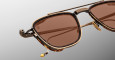 Close-up of Jacques Marie Mage 1992 sunglasses featuring stylish square frames with brown-tinted lenses, gold details, and tortoiseshell accents, set against a gradient gray background.
