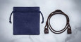 The Jacques Marie Mage 1992, featuring a blue suede drawstring pouch with embossed logo and a coiled dark brown leather strap with clasps, is displayed on a light marble surface.