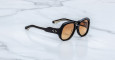 The Jacques Marie Mage Ocean Child sunglasses, featuring black thick frames, brown gradient lenses, and silver dot accents near the hinges, rest on a white marble surface.