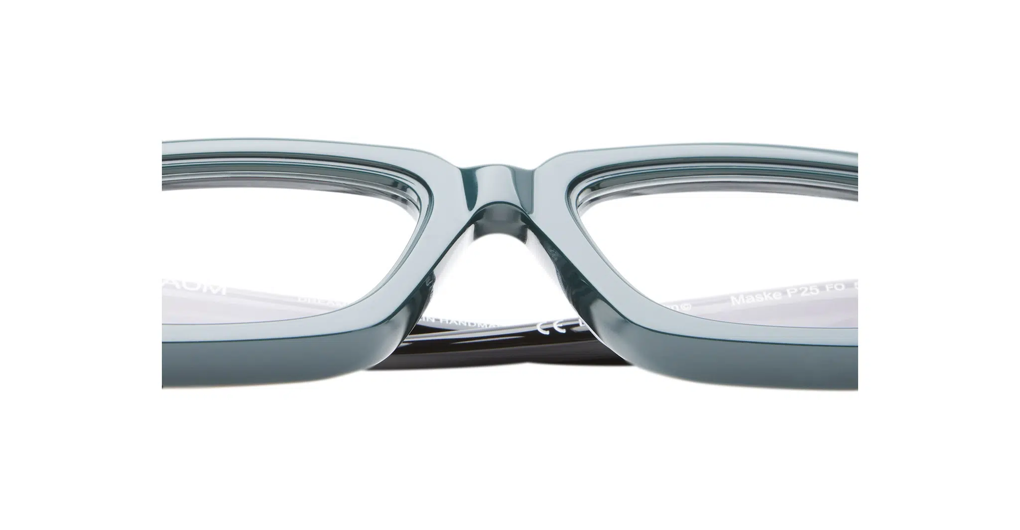 Close-up of the bridge and lenses of Kuboraum P25 teal rectangular eyeglass frames, highlighting their glossy finish and clear prescription lenses against a white background.