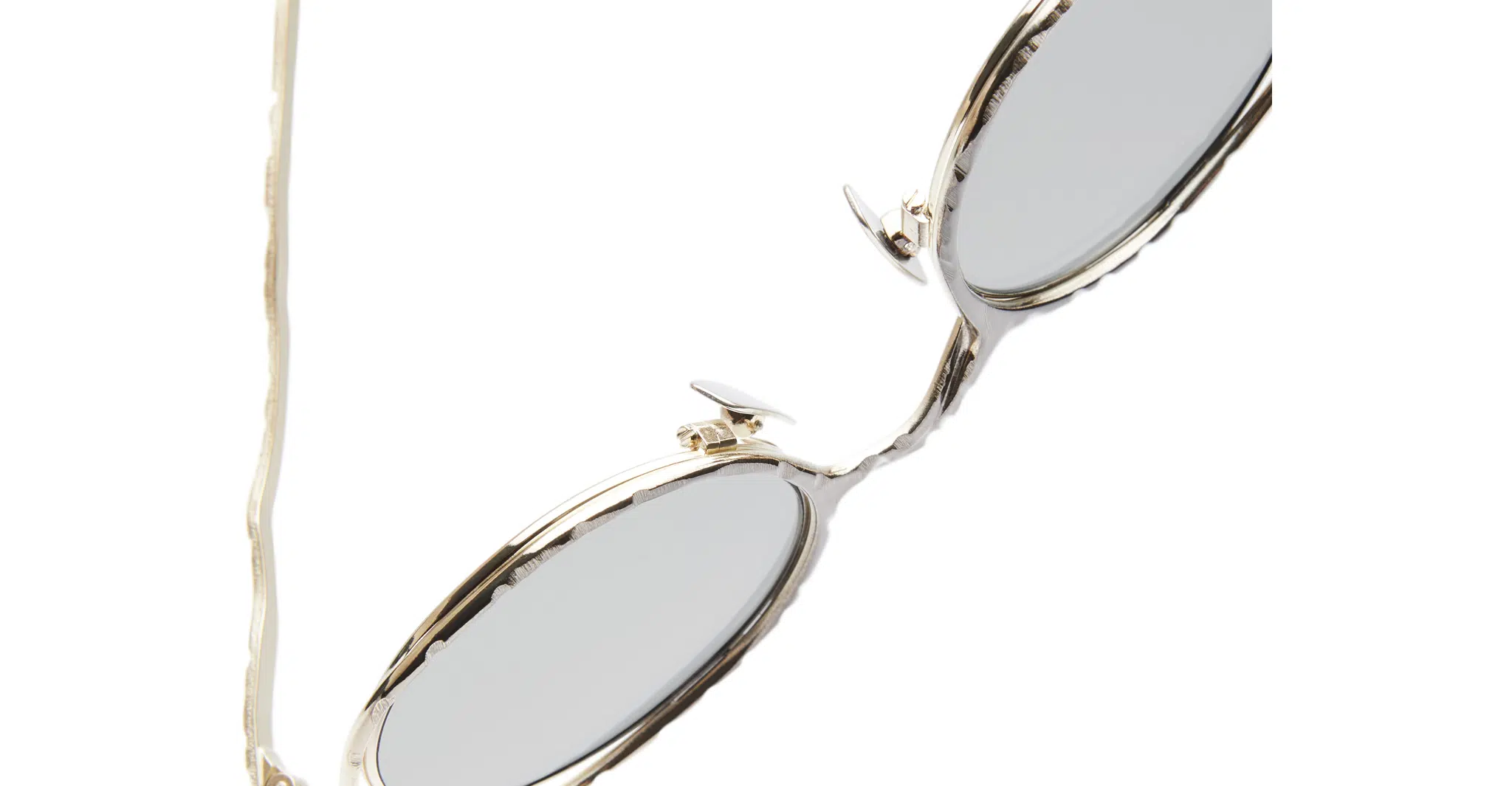 Kuboraum-H11-GMG-Gun-Metal-KRSH11GMG000002F-Detail2-Dan-Deutsch Close-up of the Kuboraum H11 oval sunglasses featuring gold metal frames and grey lenses, partially shown against a white background.