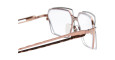 Close-up of Kuboraum H15 eyeglasses with rose gold metallic frames and clear lenses, shown from the side. The white background highlights their geometric design and shiny finish.