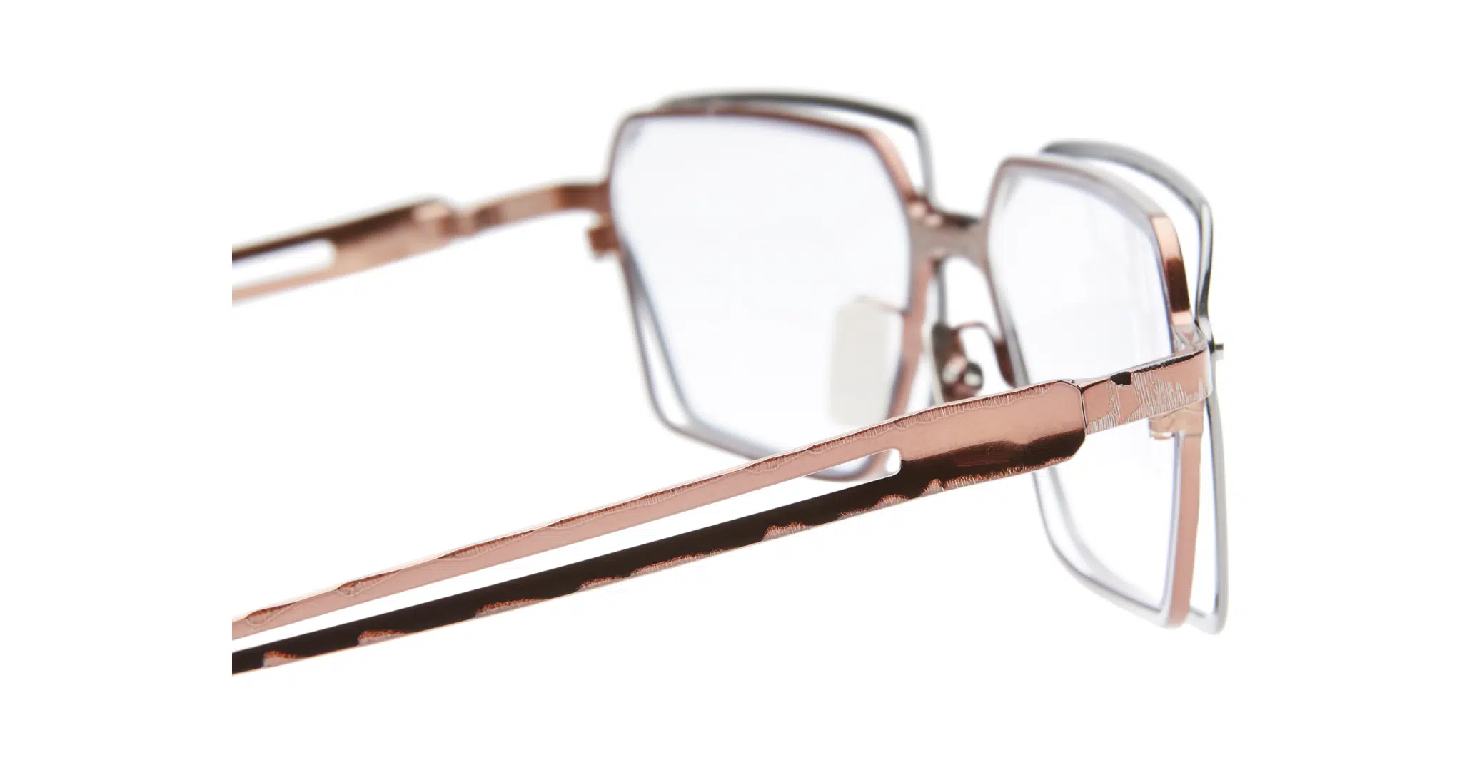 Kuboraum-H15-BZ-Gun-Metal-Optical-KROH15BZ000000OP-Detail1-Dan-Deutsch Close-up of Kuboraum H15 eyeglasses with rose gold metallic frames and clear lenses, shown from the side. The white background highlights their geometric design and shiny finish.