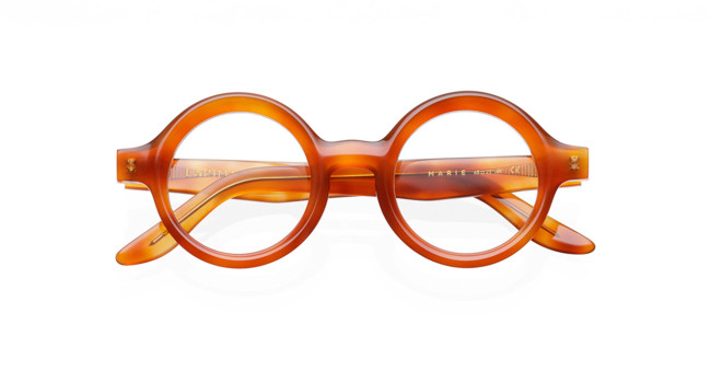The Lapima Marie eyeglasses feature round, thick translucent amber frames, shown front-facing with the arms crossed behind.