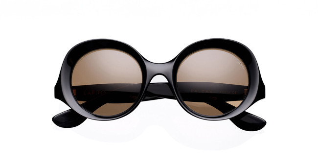 The Lapima Paloma, a pair of oversized round sunglasses with black frames and brown-tinted lenses, is displayed against a white background.