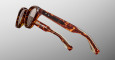 Close-up of Jacques Marie Mage Clemens eyeglasses featuring brown tortoiseshell-patterned thick frames and round lenses, photographed against a plain gradient background.
