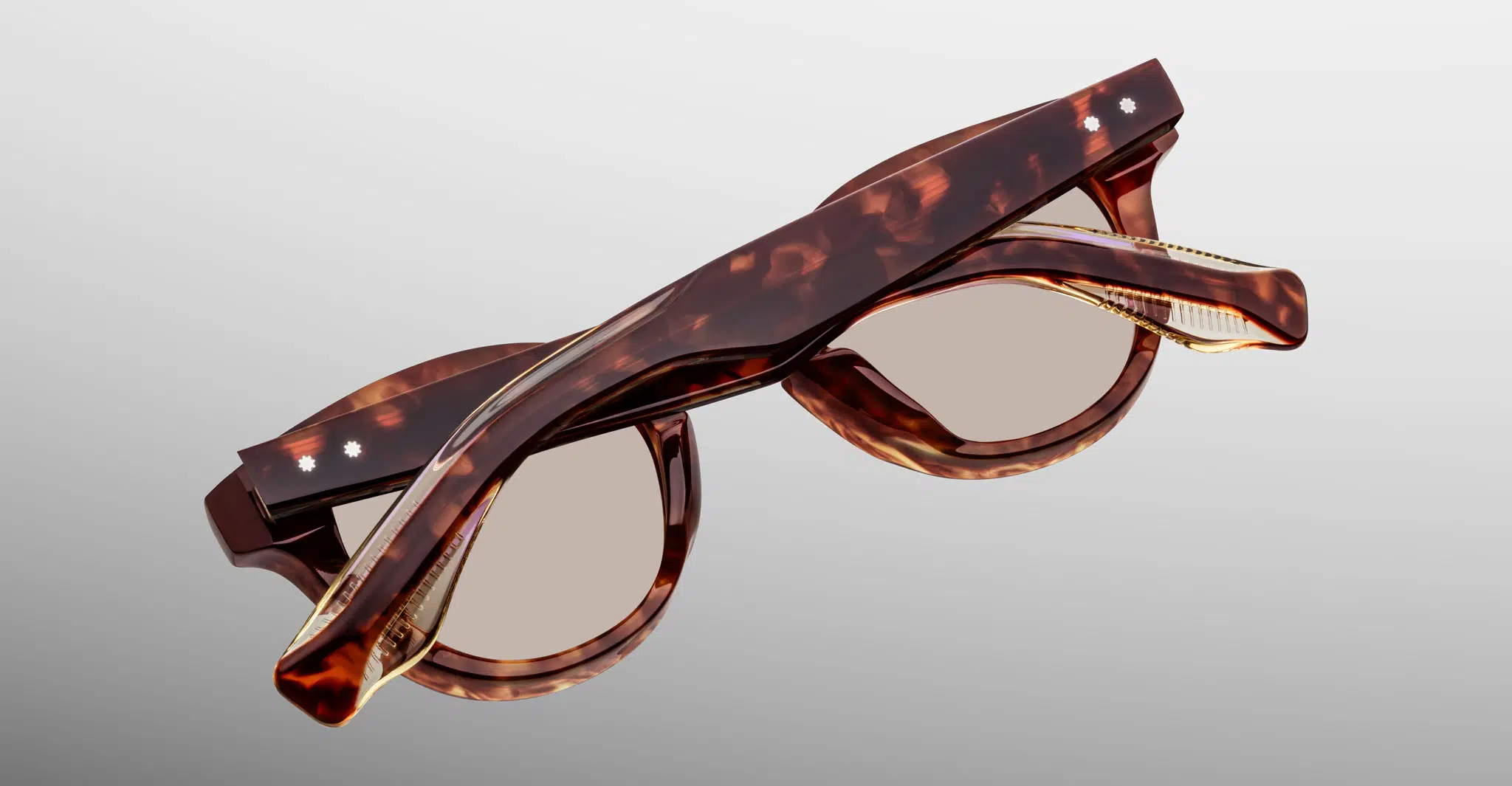 The Jacques Marie Mage Clemens eyeglasses, featuring a tortoiseshell pattern with round lenses and gold detailing, are shown folded against a light gray background.
