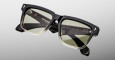 Jacques Marie Mage Hyannis black and gold square sunglasses with green-tinted lenses, shown on a light gray background. The glossy frame features brand markings on the inside of the arms.