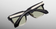 The Jacques Marie Mage Hyannis sunglasses feature thick black frames, gold accents, and light green lenses, shown folded on a light gray background.
