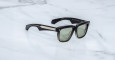 The Jacques Marie Mage Hyannis is a pair of black rectangular sunglasses with green tinted lenses and silver temple accents, shown resting on a white marble surface.