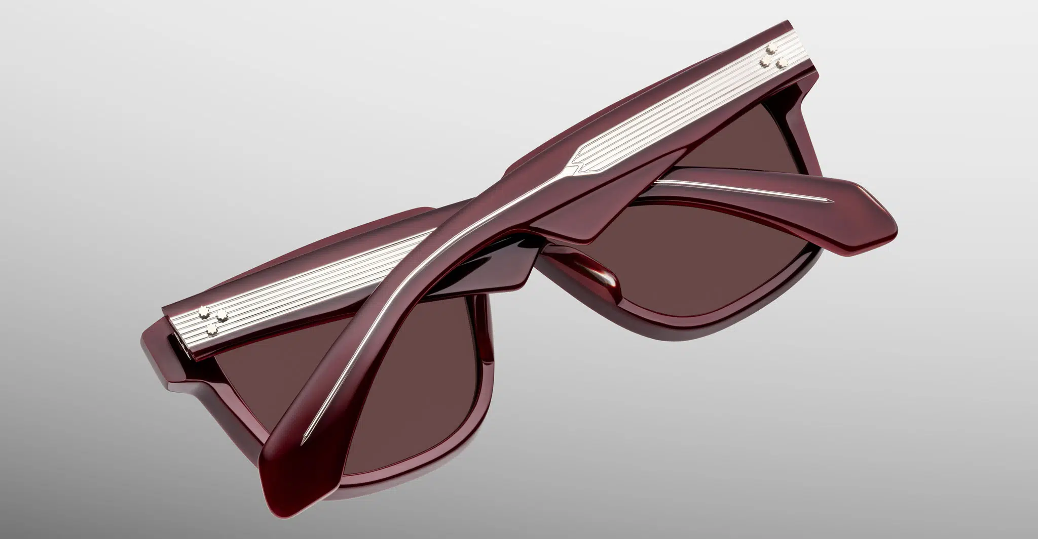 A pair of Jacques Marie Mage Hyannis sunglasses in stylish dark red, featuring thick frames and silver accents, folded and viewed from above on a light gray background.