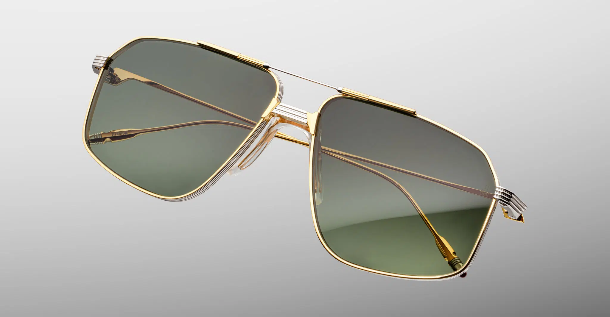 Jacques-Marie-Mage-Jagger-Musket-JMMJG-12M-Detail1-Dan-Deutsch The Jacques Marie Mage Jagger sunglasses feature stylish aviator gold metal frames and green-tinted lenses, showcased on a plain light gray background.