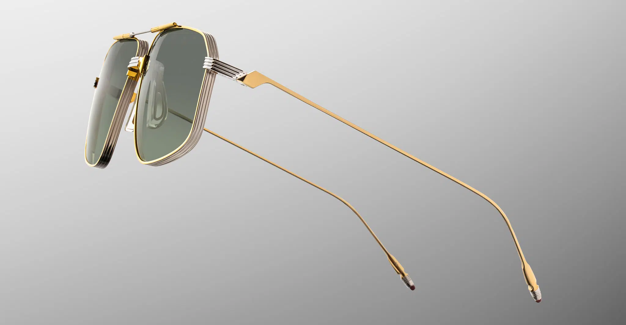 Jacques-Marie-Mage-Jagger-Musket-JMMJG-12M-Detail2-Dan-Deutsch The Jacques Marie Mage Jagger features green-tinted rectangular lenses and slim gold metal frames and arms, showcased against a gradient gray background.
