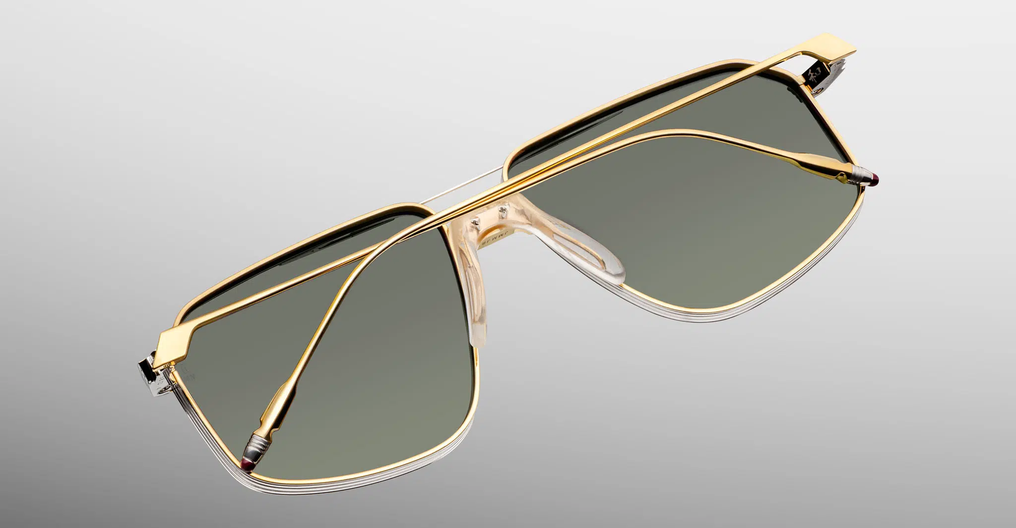 Jacques-Marie-Mage-Jagger-Musket-JMMJG-12M-Detail3-Dan-Deutsch Jacques Marie Mage Jagger aviator sunglasses feature gold rims, green-tinted lenses, clear nose pads, and slim metal temples, displayed against a light gray background.