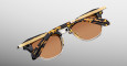 The Jacques Marie Mage Sartre sunglasses feature a tortoiseshell-patterned frame with ornate gold detailing on the arms, shown partly folded against a gradient gray background.