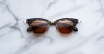 The Jacques Marie Mage Sartre tortoiseshell sunglasses with brown lenses rest on a white marble surface.