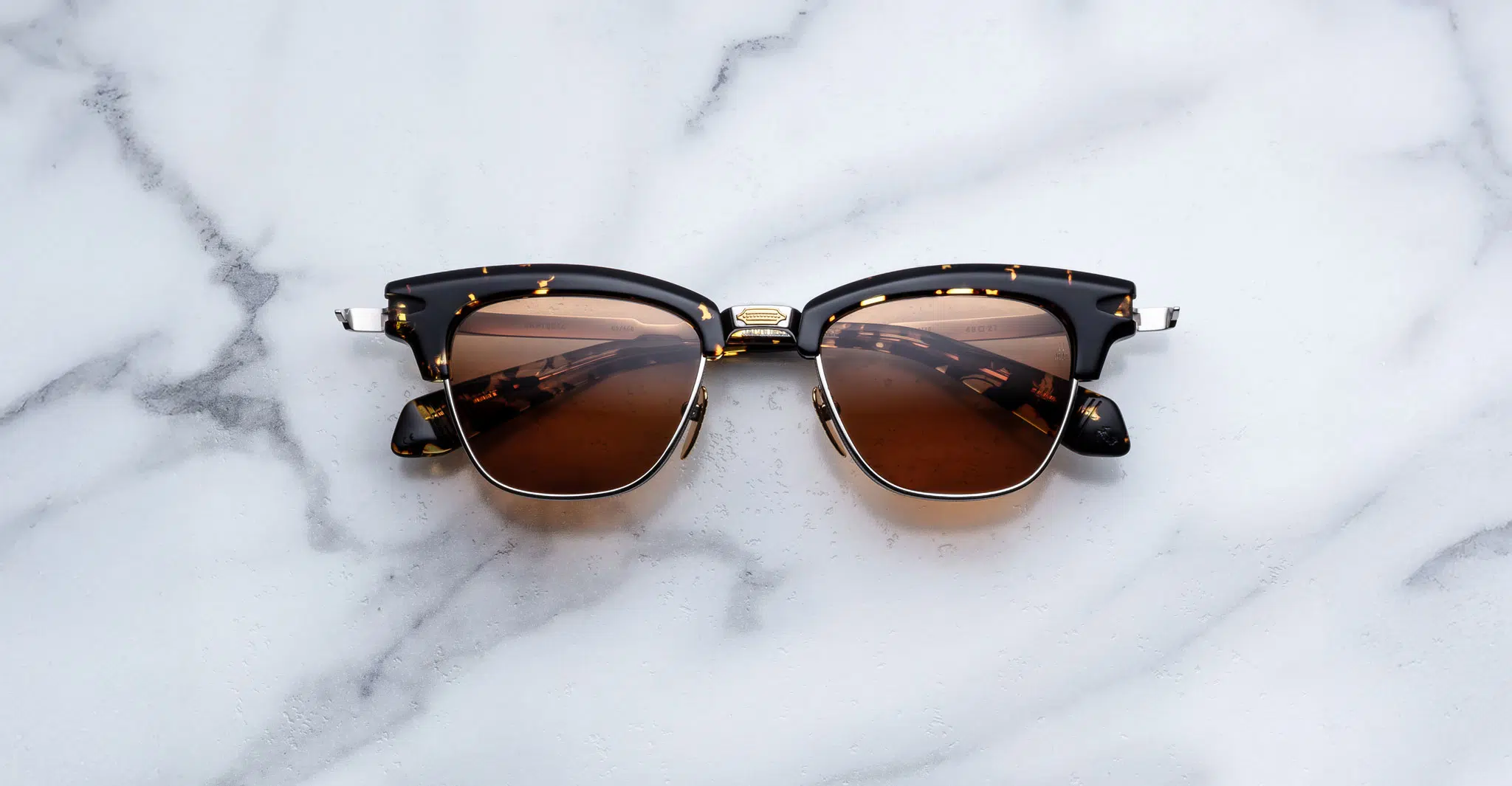 The Jacques Marie Mage Sartre tortoiseshell sunglasses with brown lenses rest on a white marble surface.