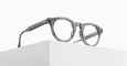 The Matsuda M1036 (Copy) round eyeglasses feature thick, transparent gray frames and are displayed atop a white geometric block against a minimalist white background.