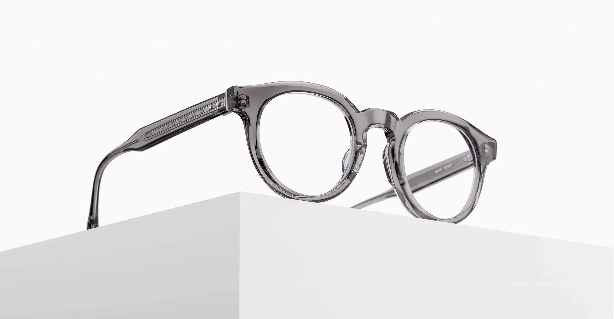 The Matsuda M1036 (Copy) round eyeglasses feature thick, transparent gray frames and are displayed atop a white geometric block against a minimalist white background.
