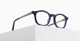 The Matsuda M2068 eyeglasses, featuring dark frames and gold, patterned arms, rest on the edge of a white minimalist surface against a plain, light background.