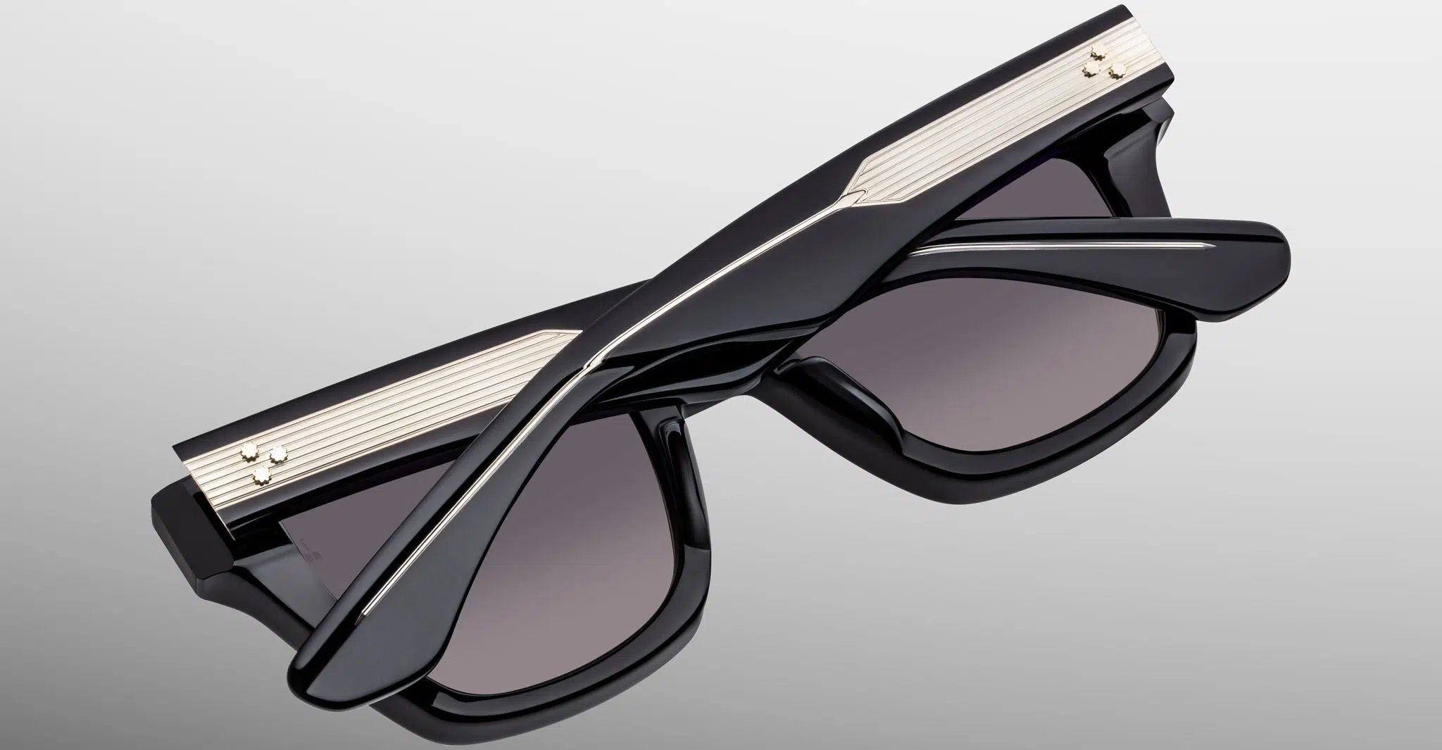 The Jacques Marie Mage Torrance sunglasses, in black with gold metallic details, are shown folded on a light gray background, highlighting their distinctive arm design and dark tinted lenses.