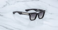 The Jacques Marie Mage Torrance sunglasses are black, rectangular with gradient dark lenses and thick arms accented by a silver detail, shown on a white marble surface.