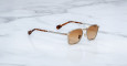 The Jacques Marie Mage Beckett is a pair of square, light brown sunglasses with silver frames and tortoiseshell-patterned arms, displayed on a white marble surface.